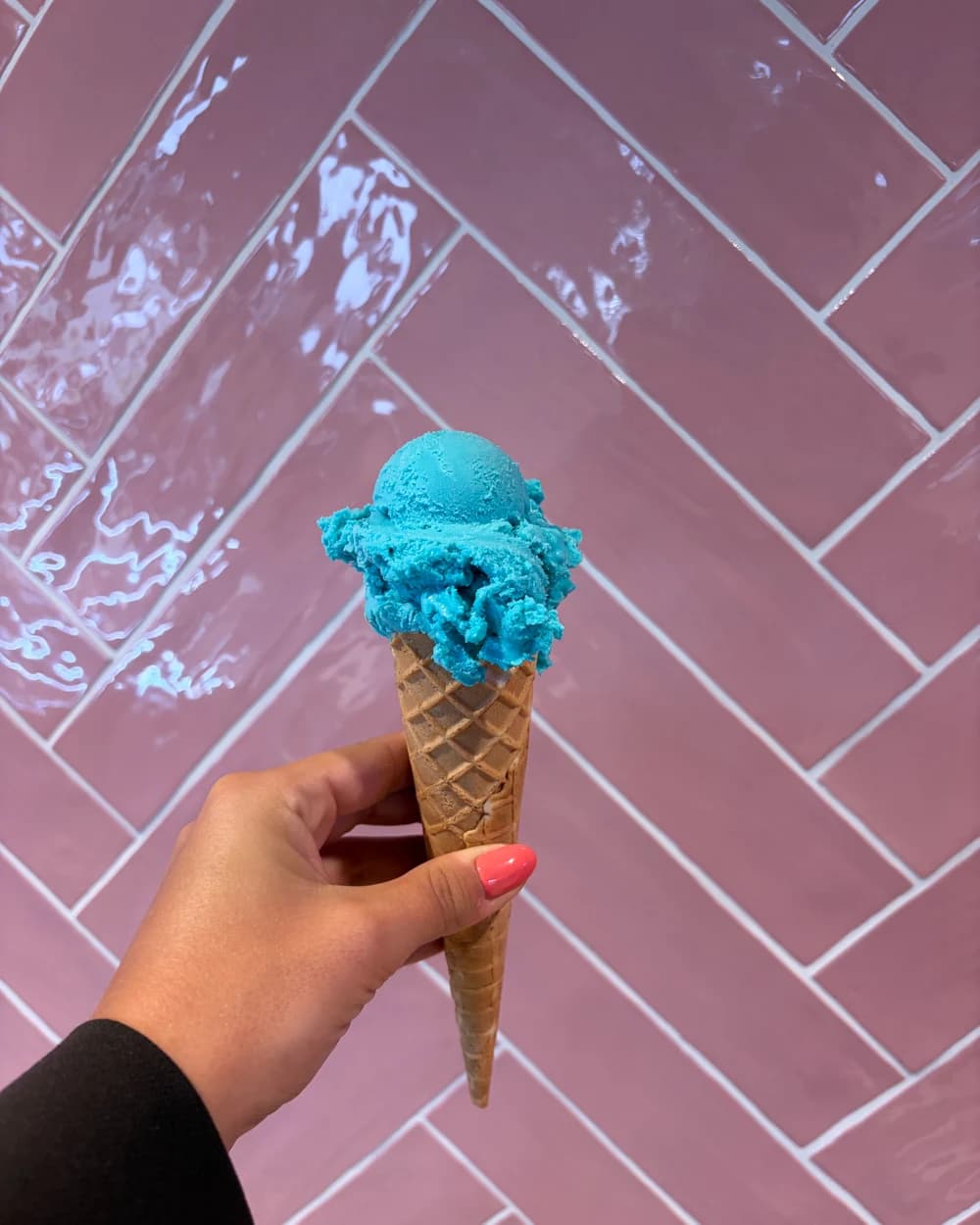 Een hoorntje blauw ijs van IJssalon Zoet den Eelder tegen de roze tegelwand