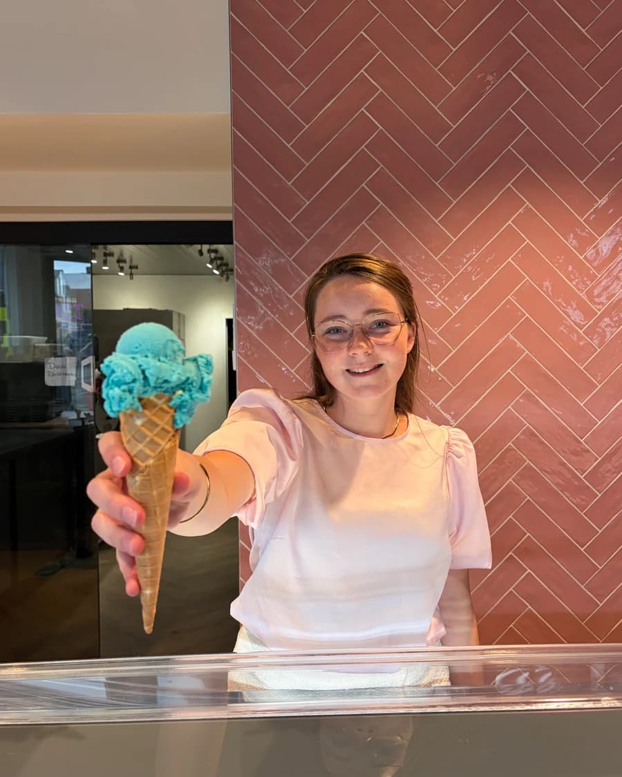 Een medewerker reikt een hoorntje ijs aan over de vitrine